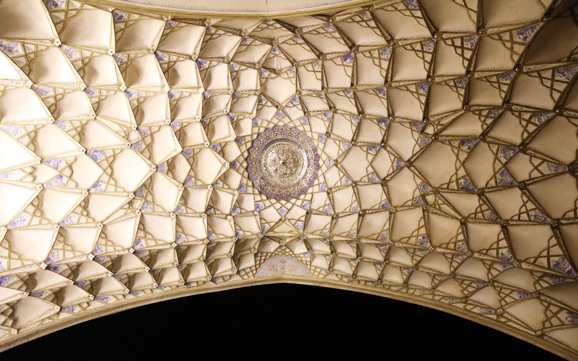 Intricate Āina-kāri (mirror work) ceiling of Khaneh Ameri in Kashan, featuring geometric star patterns, gold outlines, and a circular mirrored medallion at the centre.