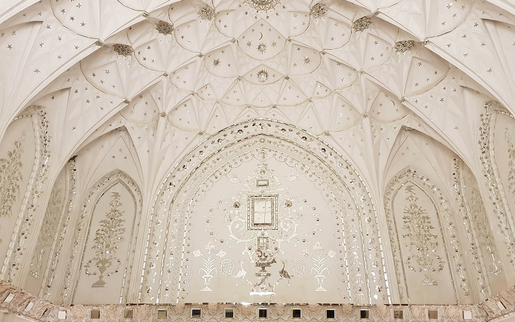 Subtle mirror work in the ceiling of Tabatabaie House, Kashan — pale geometric star patterns and finely inlaid details framing a softly ornamented central wall panel.