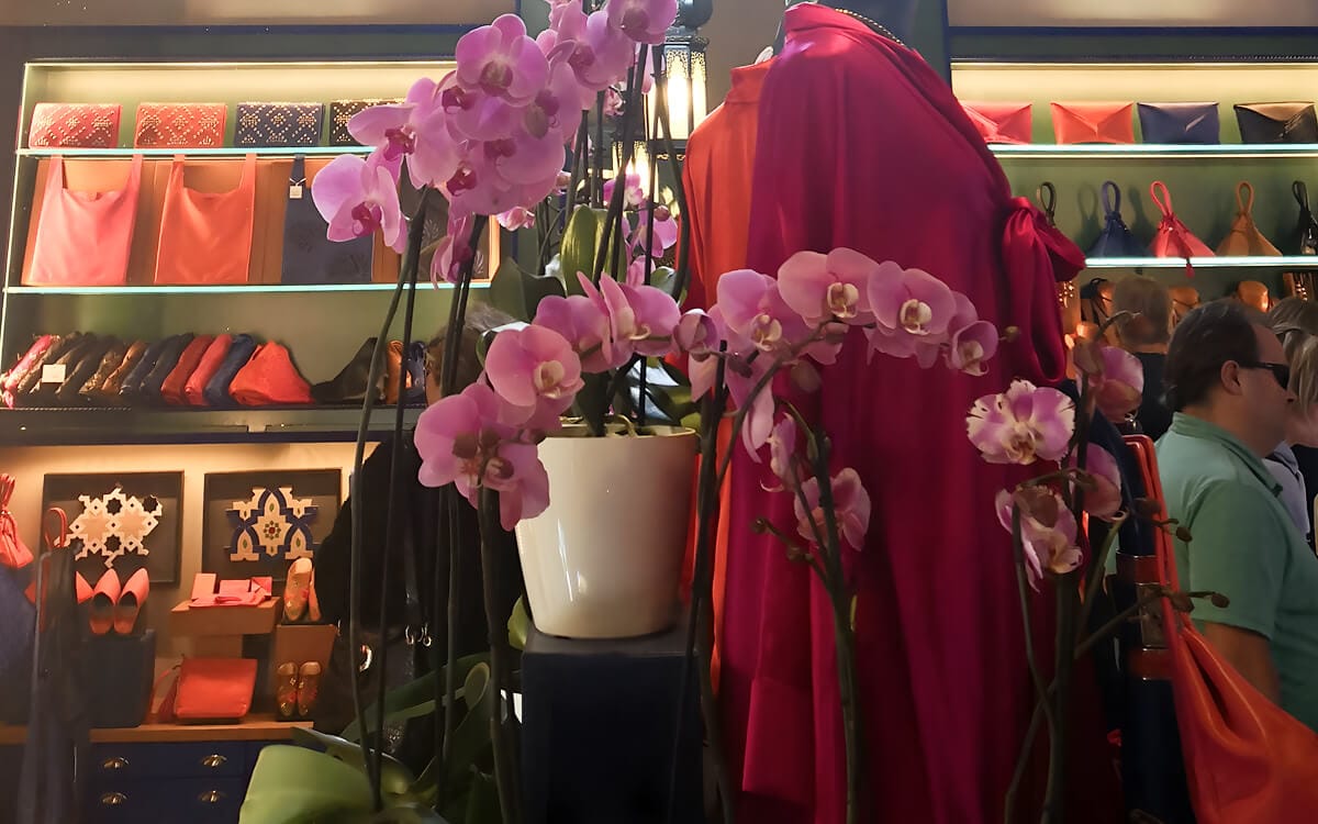 Jardin Majorelle shop interior with colorful bags, shoes, and a flowing garment displayed among orchids and warm lighting