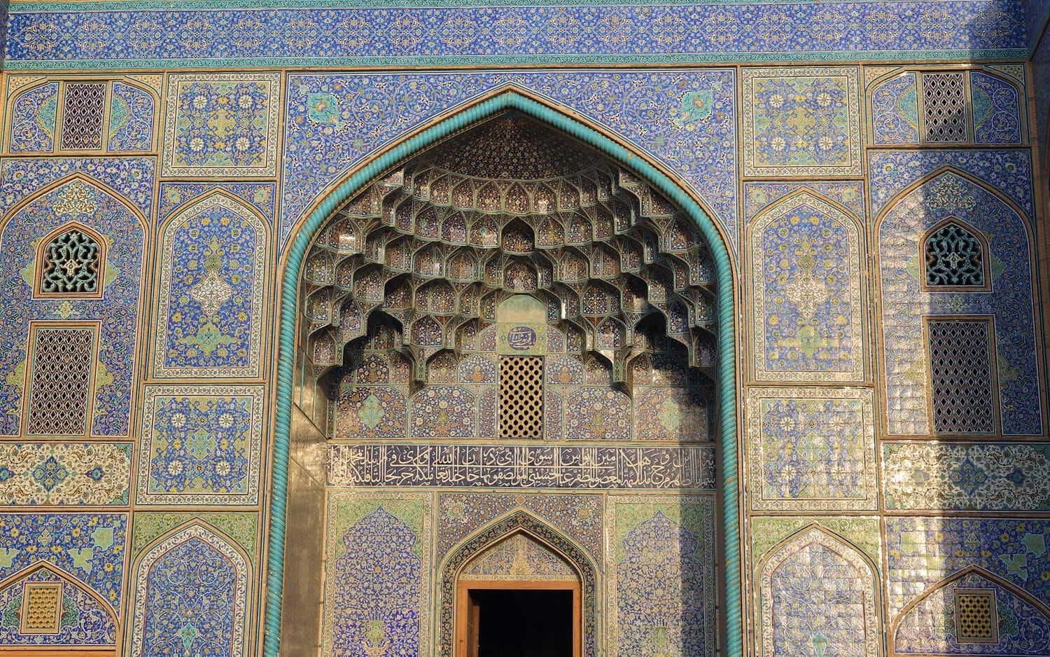 The intricately tiled entrance façade of Sheikh Lotfollah Mosque in Isfahan, featuring layered muqarnas and detailed blue-turquoise floral patterns around a pointed archway.