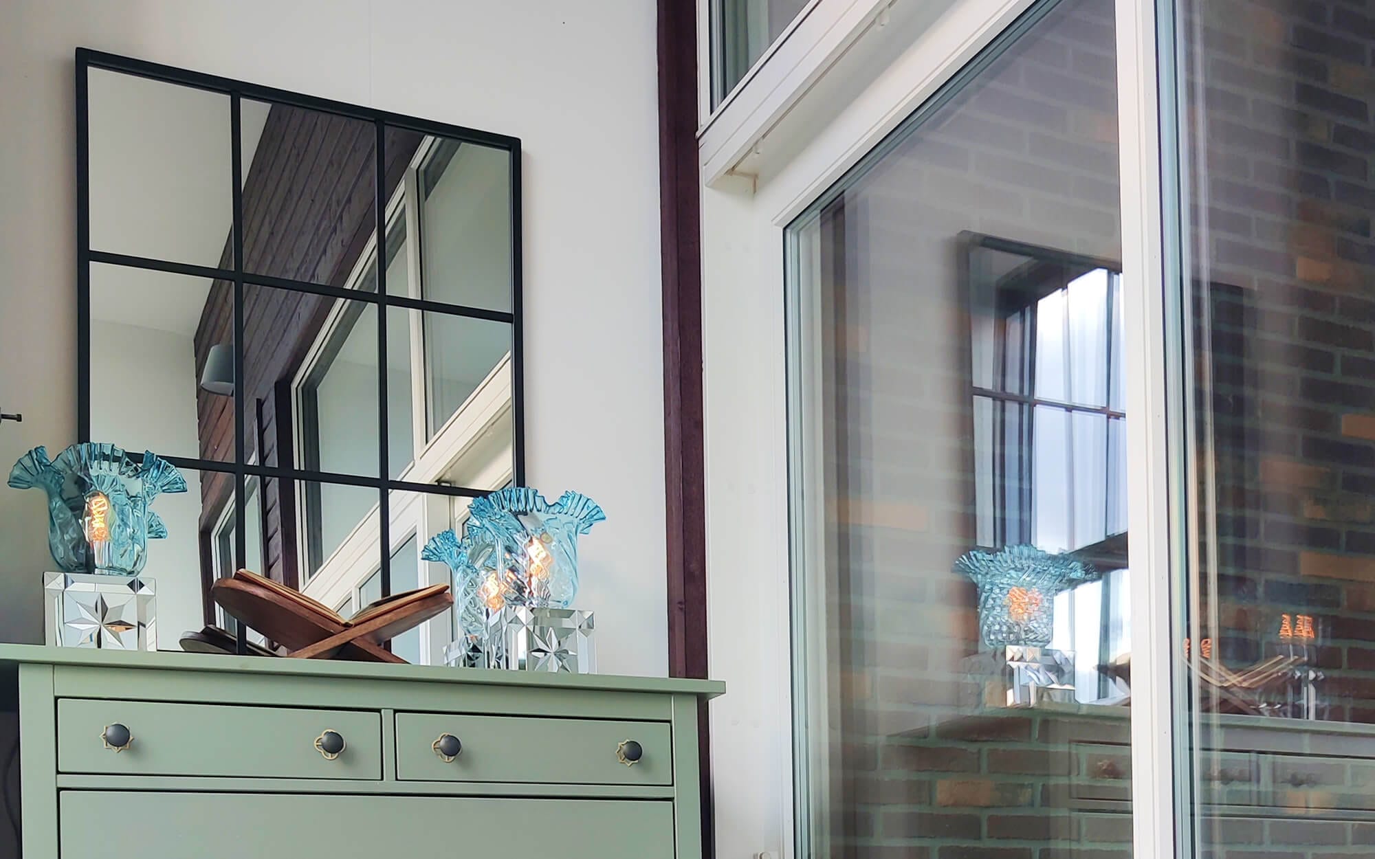 Modern home interior with black framed mirror and two mirrored table lamps (aina kari Laleh) on a green sideboard.