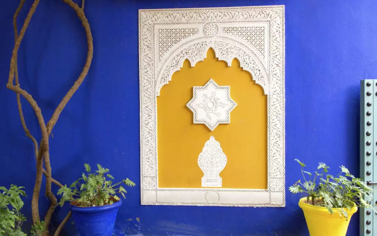 Decorative Moroccan wall niche with carved white plaster details set into a deep blue wall with potted plants