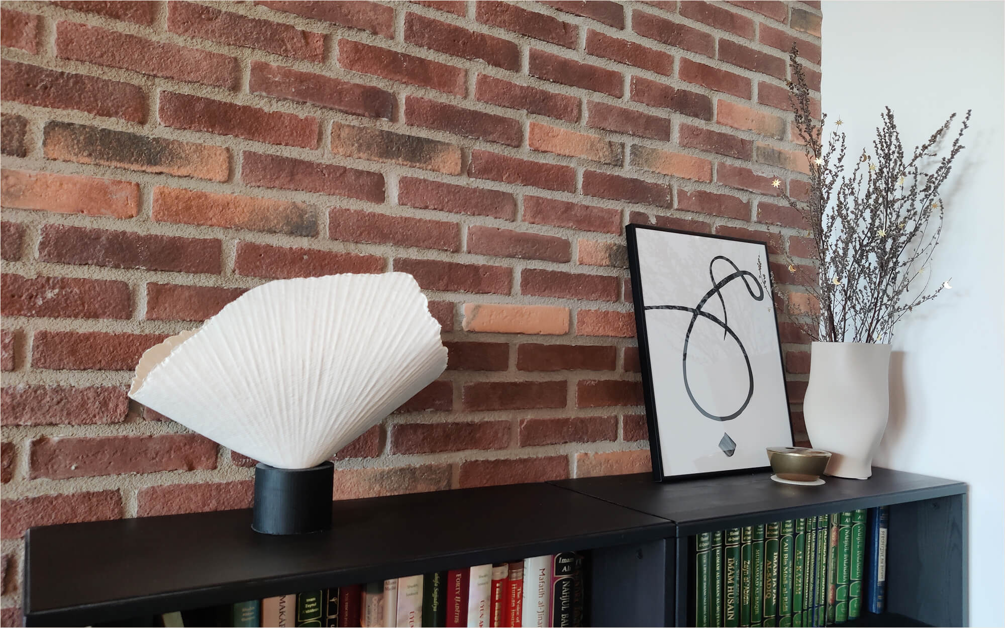 Minimal Ramadan branch decoration: dried branches adorned with small gold moon and star cutouts in a white vase, placed beside a framed minimalist calligraphy of the word “hubb” (love) in Arabic.