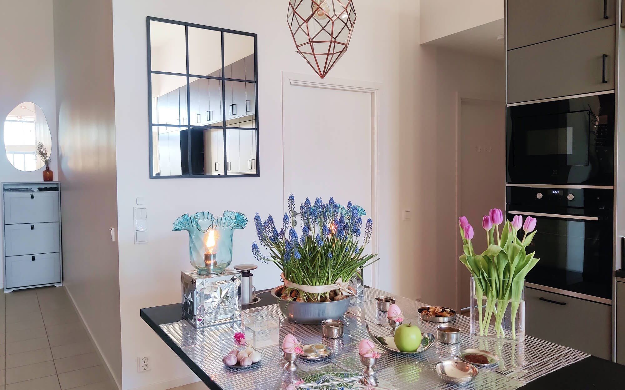 A mirrorwork (āyeneh-kāri) inspired Haftseen table set in a bright, modern kitchen, arranged on a reflective metallic surface with sonbol.