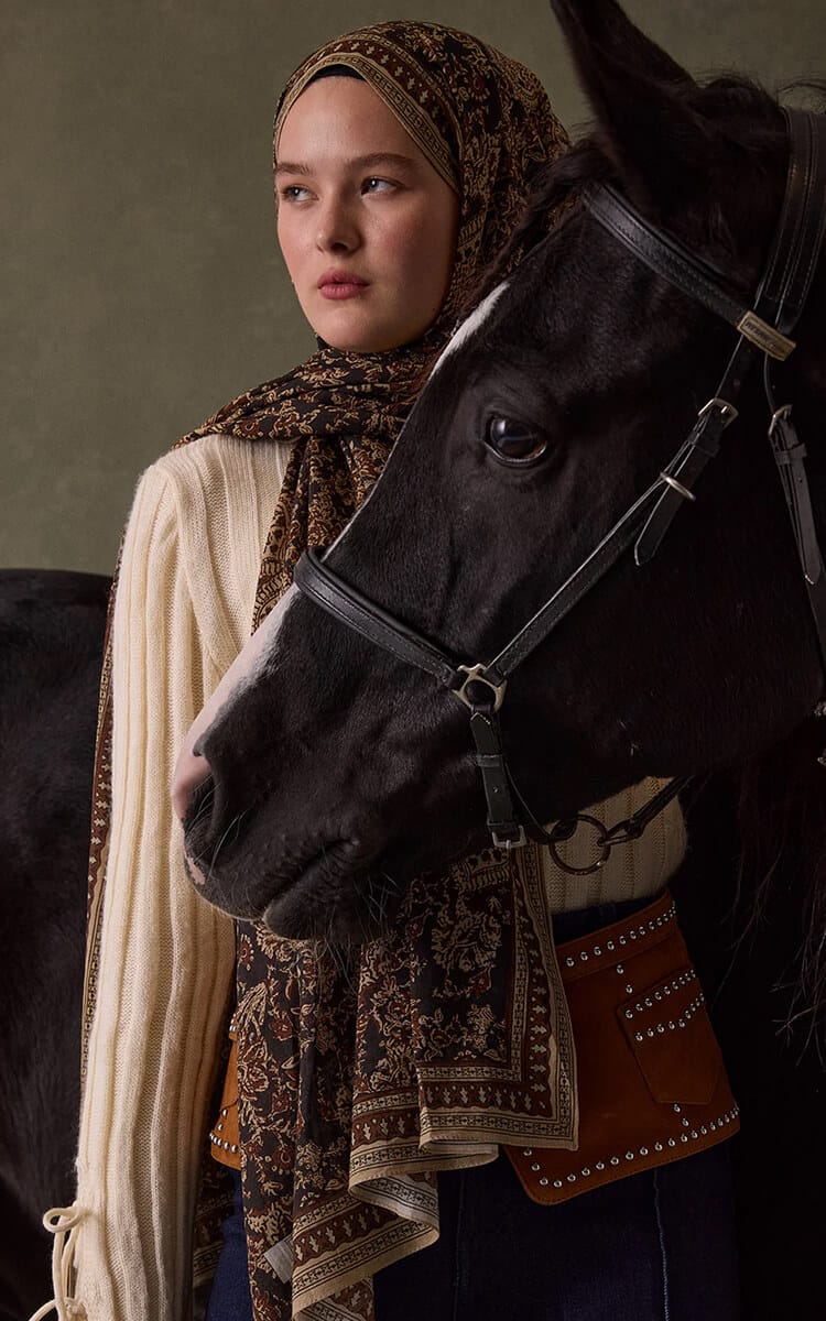 Woman in a paisley hijab standing beside a black horse.