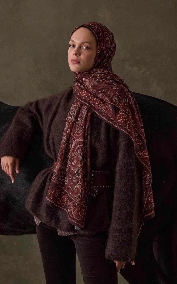 Woman wearing a burgundy paisley hijab standing beside a black horse.