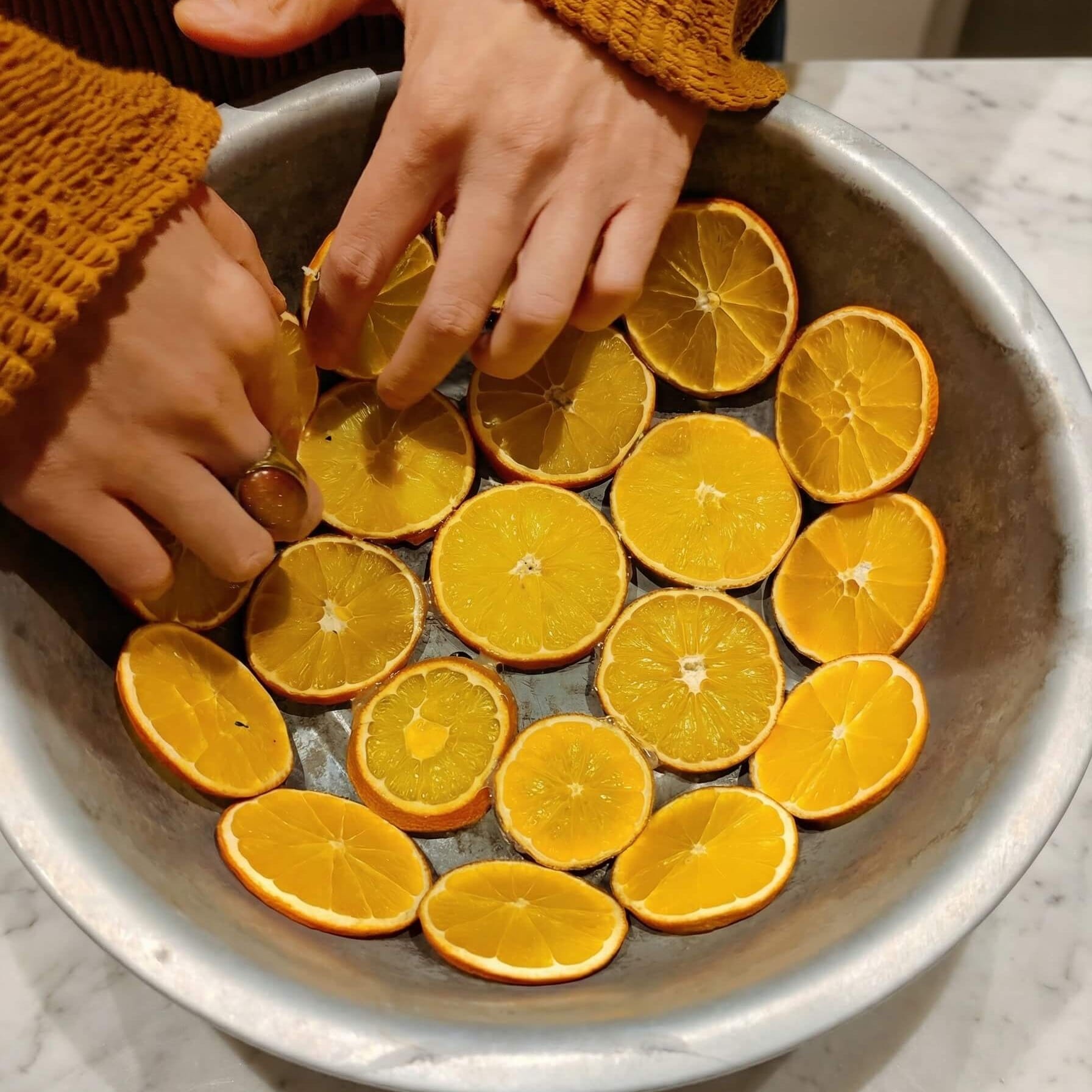 Shaping a DIY orange slice bowl by arranging dried orange slices inside a metal bowl used as a mould.