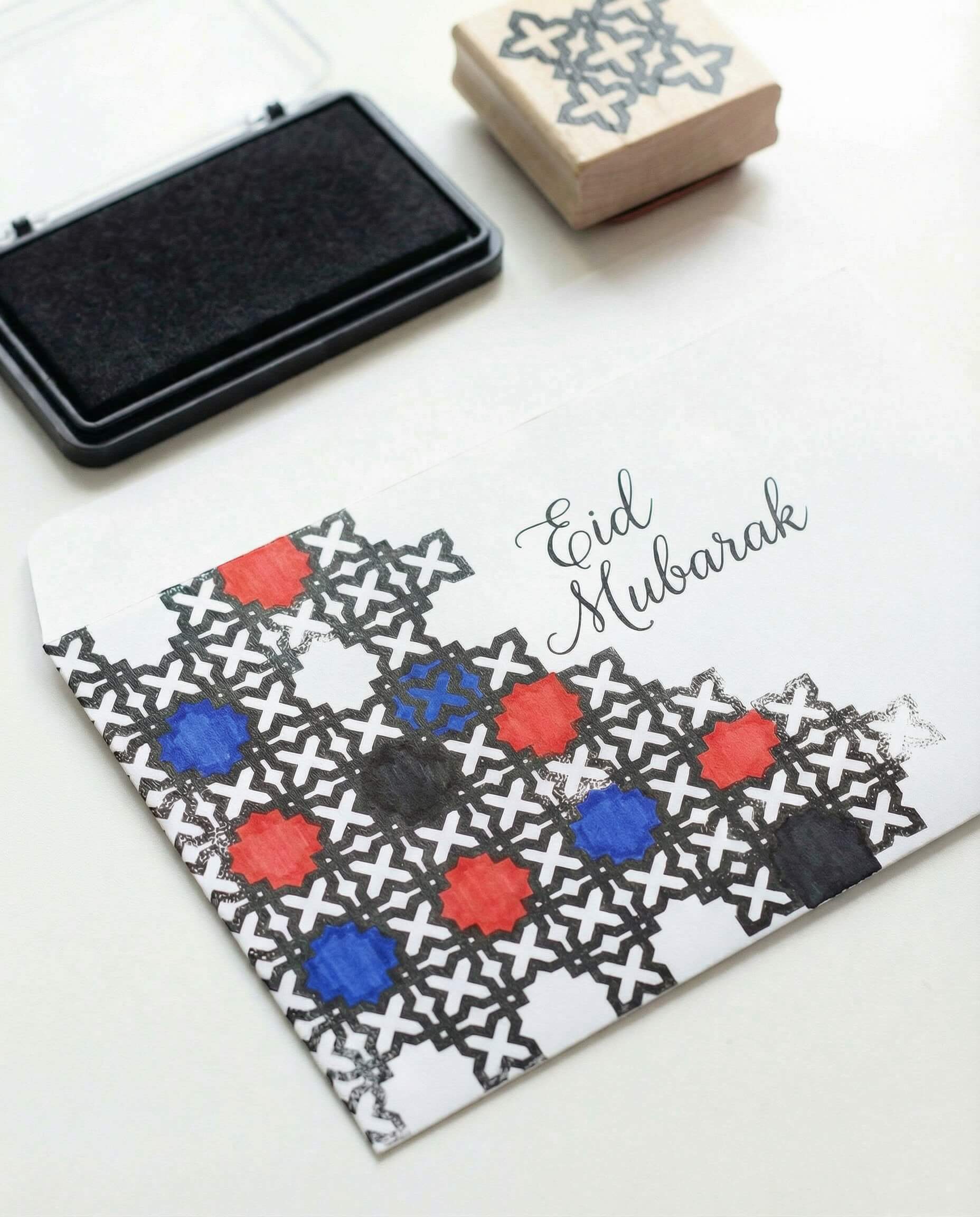 Eid money envelope decorated with a stamped Islamic geometric pattern and selectively filled shapes in red, blue, and black.