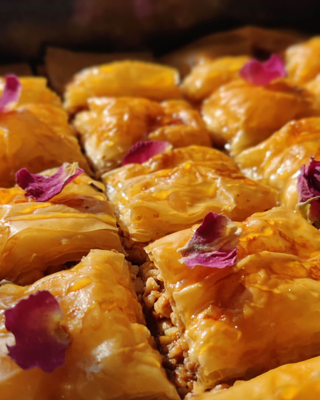 Close-up of golden baklava showing crisp phyllo layers and nut filling, topped with rose petals.