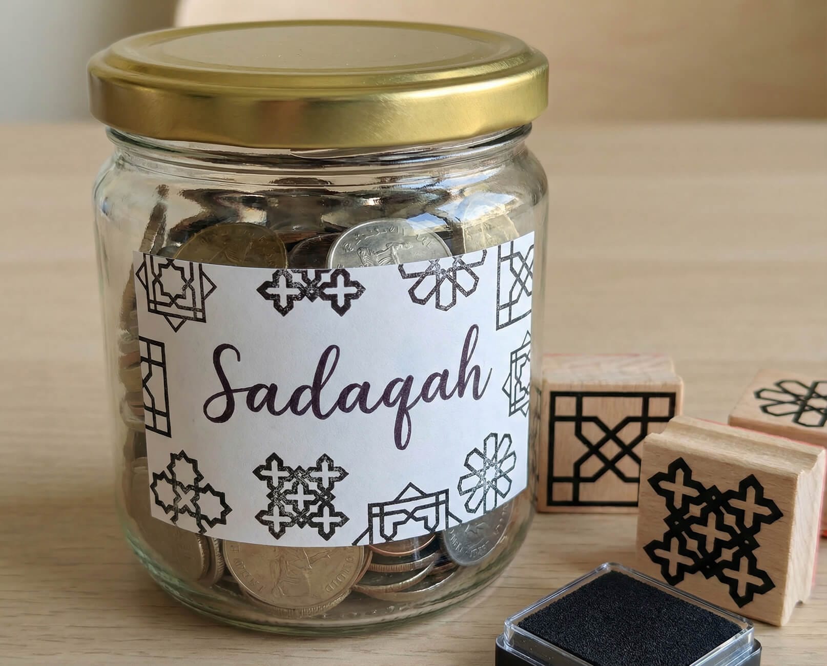 DIY Sadaqah jar with a handwritten label and Islamic geometry stamp patterns, designed as a meaningful Ramadan activity.