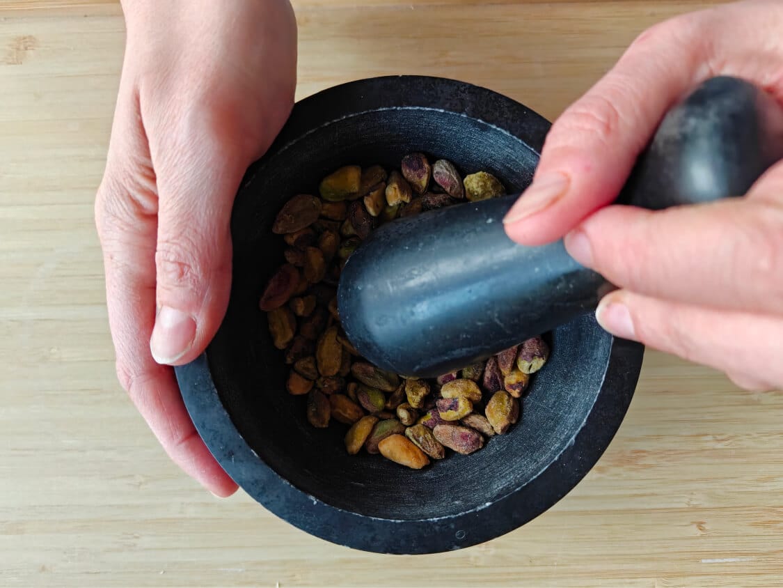 Crushing pistachios in a mortar and pestle to prepare for chocolate kataifi salami.