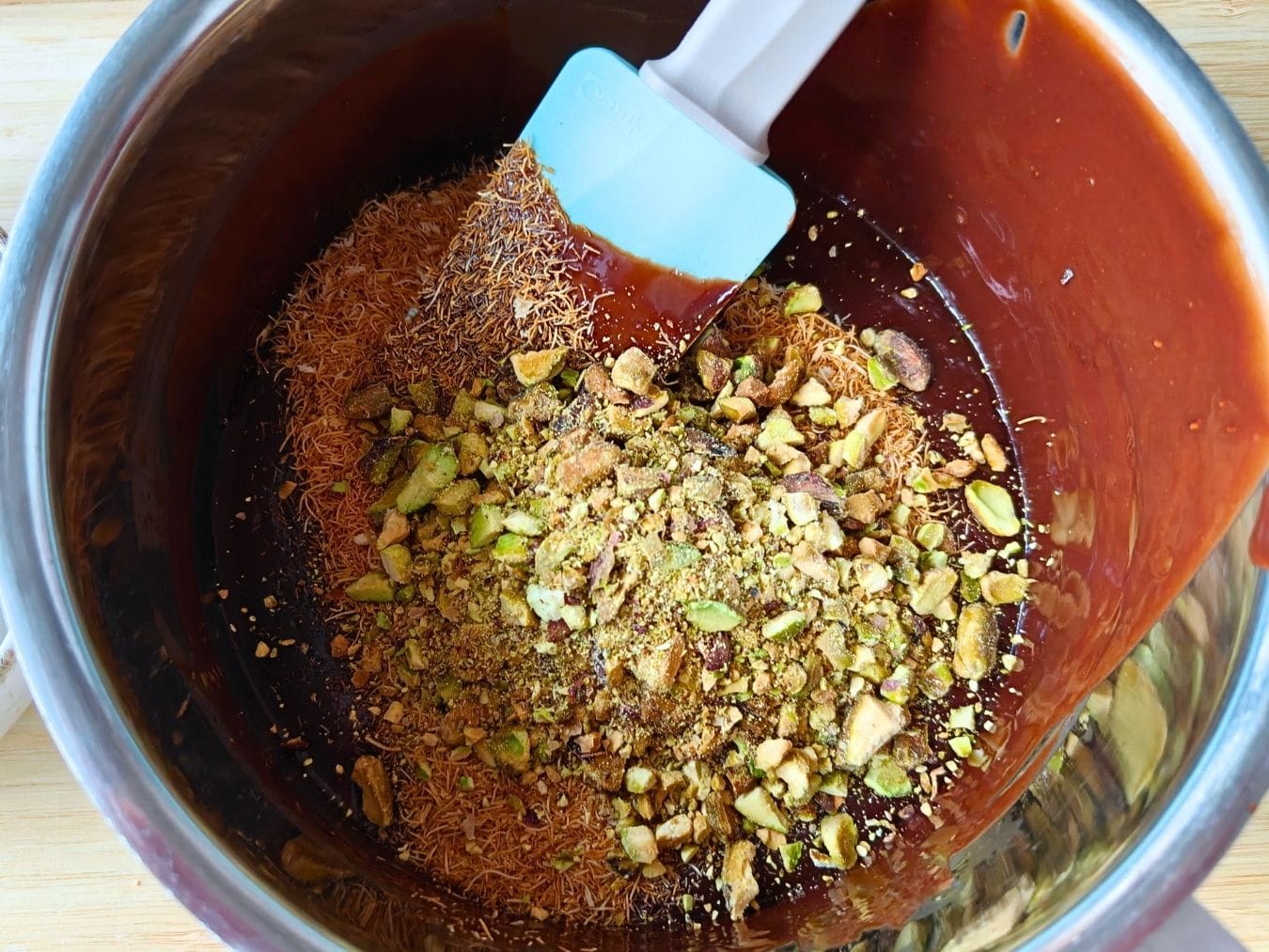 Folding toasted kataifi pastry and crushed pistachios into melted chocolate mixture for chocolate kataifi salami.