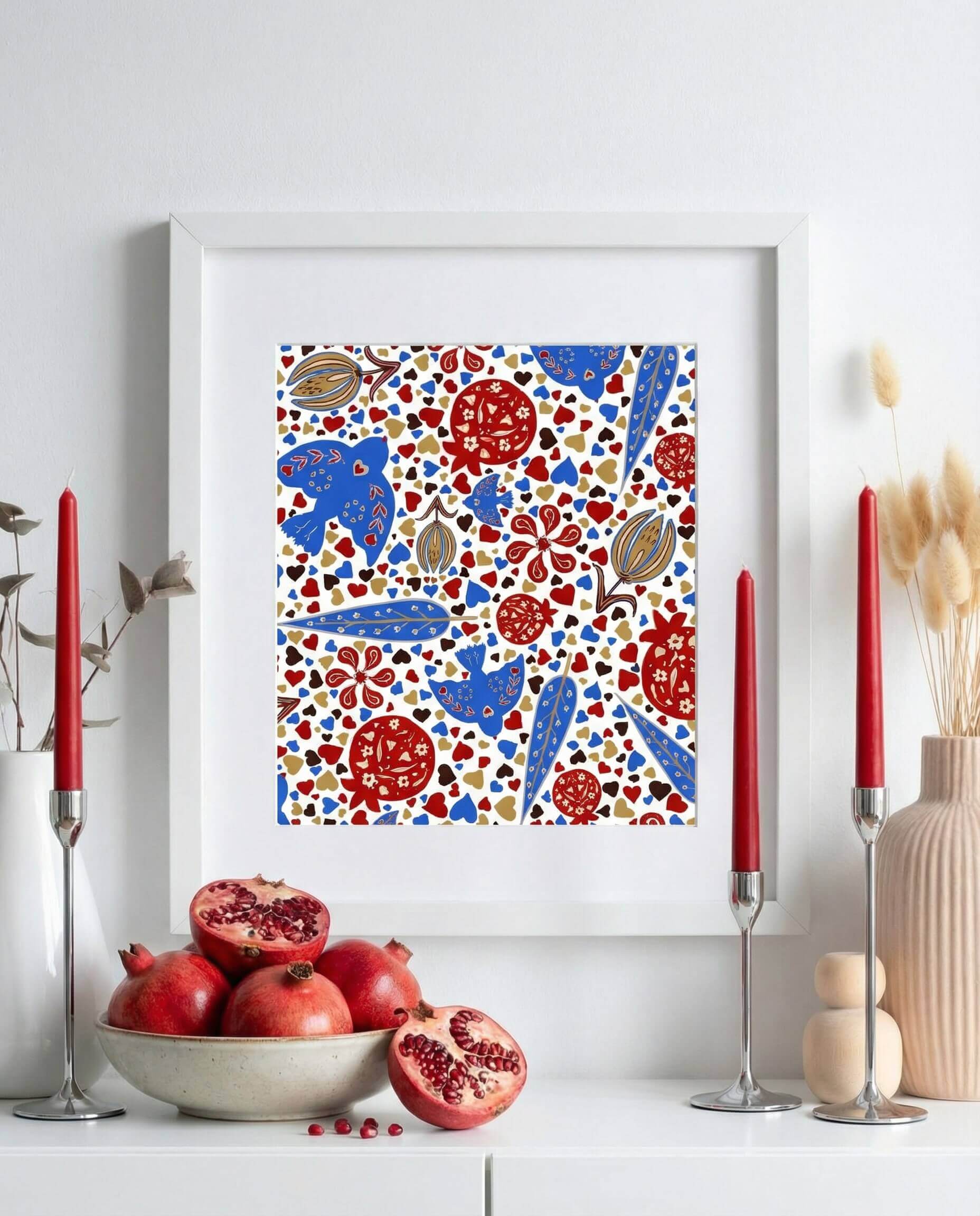 Framed Persian pomegranate and bird art print styled above a white console with fresh pomegranates and red candles, inspired by a Yalda night decor setting.