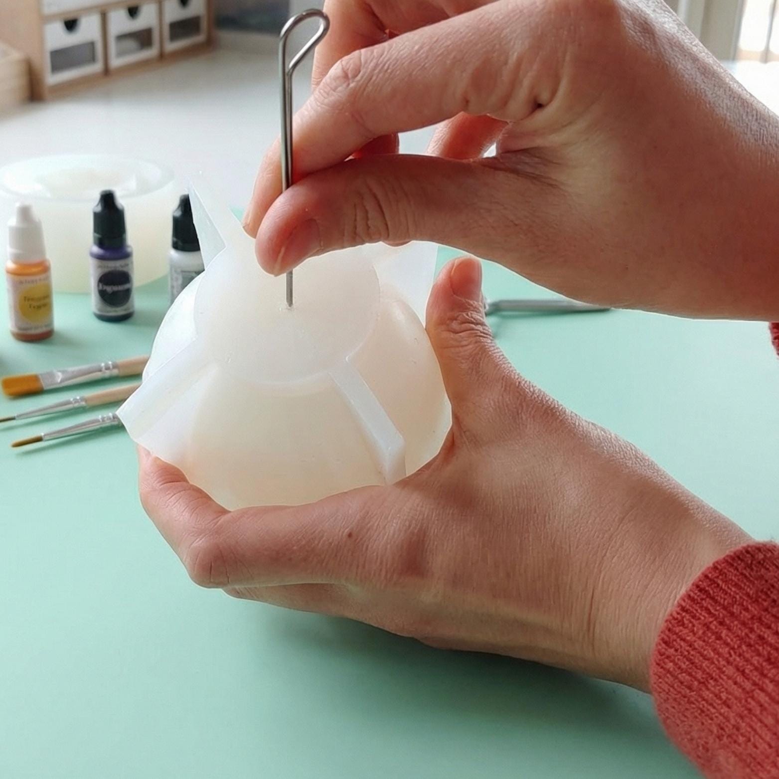 Using a metal tool to gently pierce a small hole in a silicone candle mold to insert the wick for a beeswax Ramadan candle.
