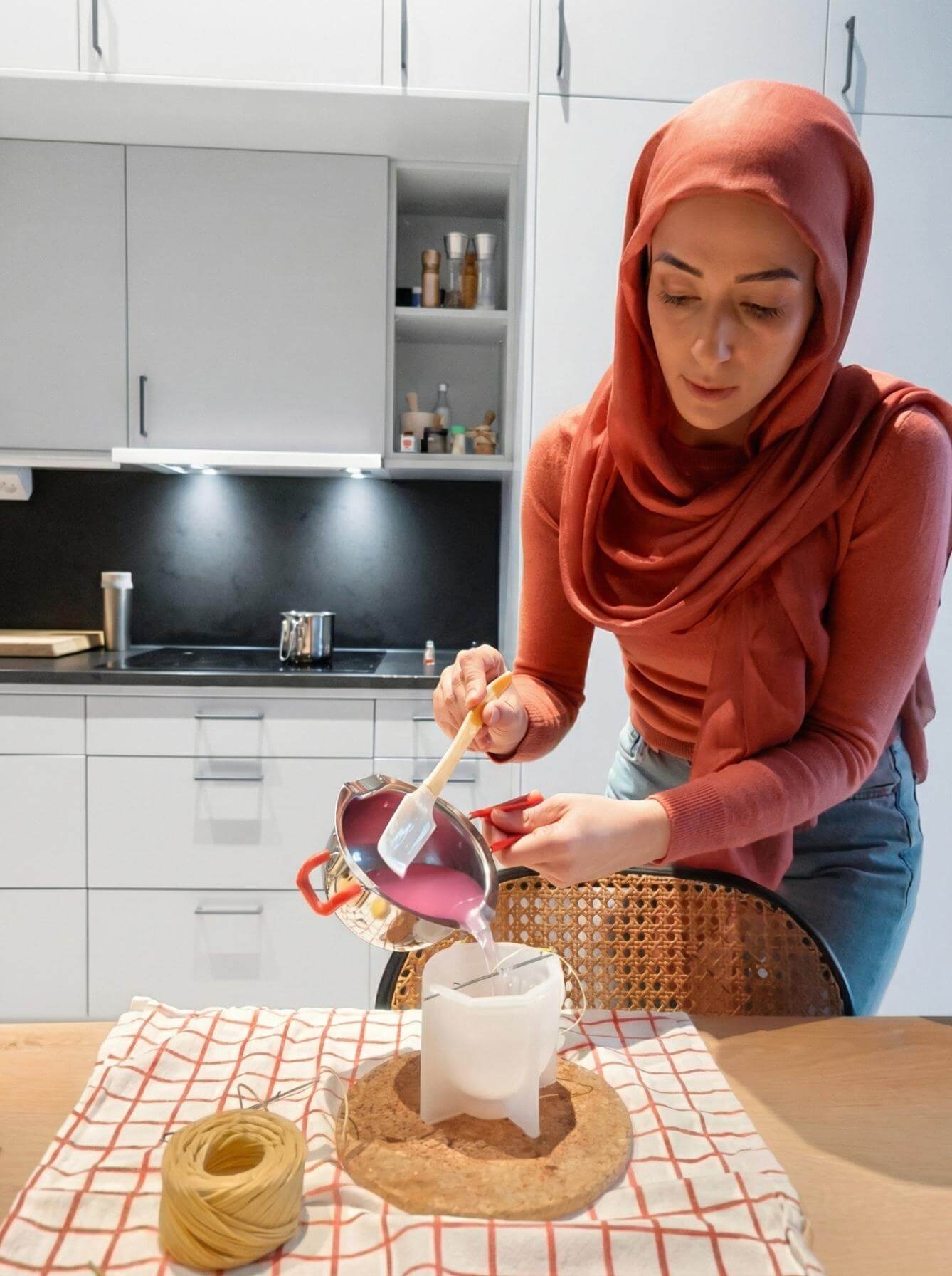Pouring melted beeswax into a silicone mold to make a DIY Ramadan candle, with wick centered and double boiler setup on the table.
