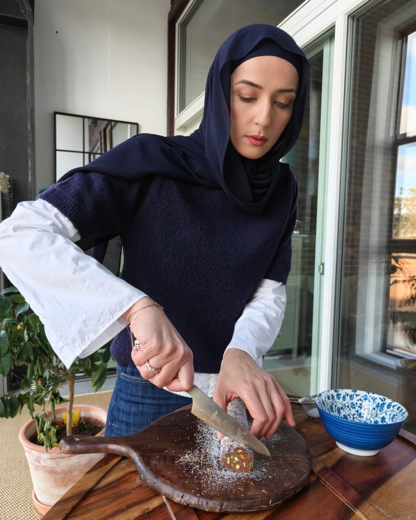 Slicing chocolate kataifi salami with pistachios on a wooden board in natural light