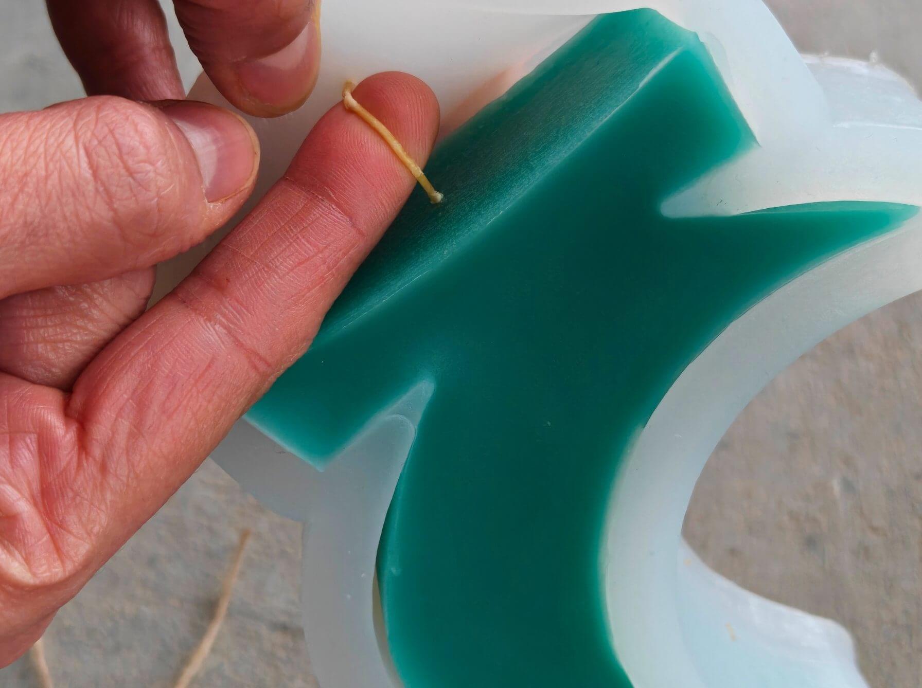 Pulling a cotton wick easily through a silicone mold after the beeswax crescent candle has fully set.