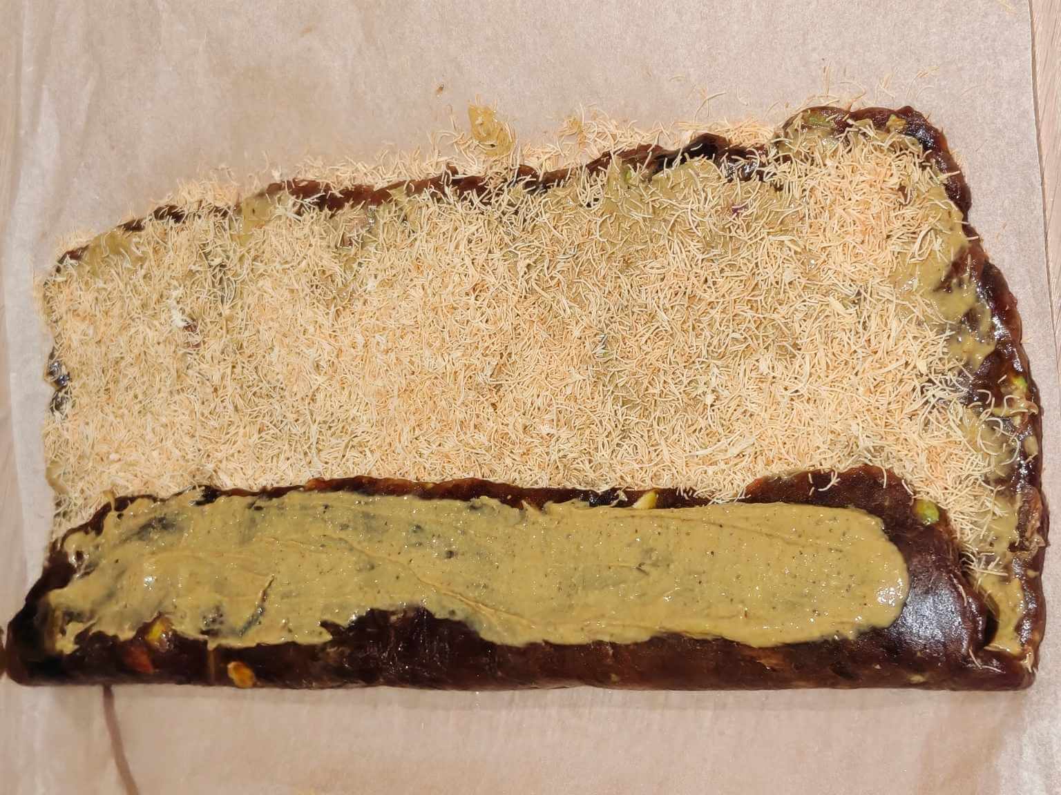 rolling pistachio date dessert with nut butter and kataifi into a log