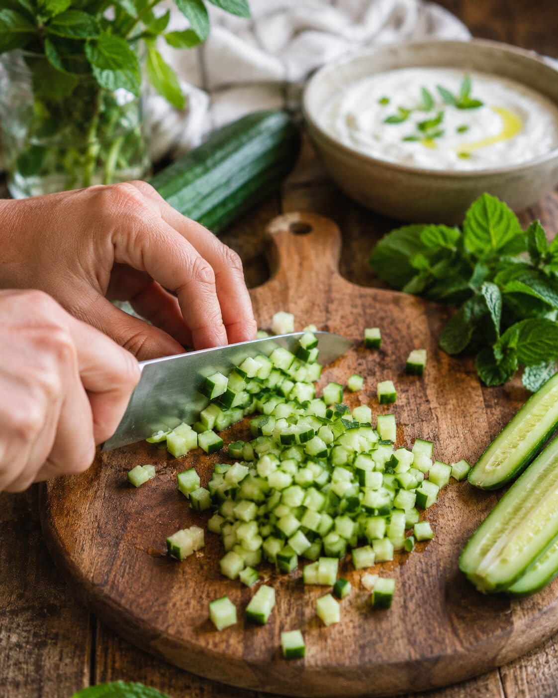 Cucumber with the skin left on being finely chopped for mast o khiar yogurt dip.