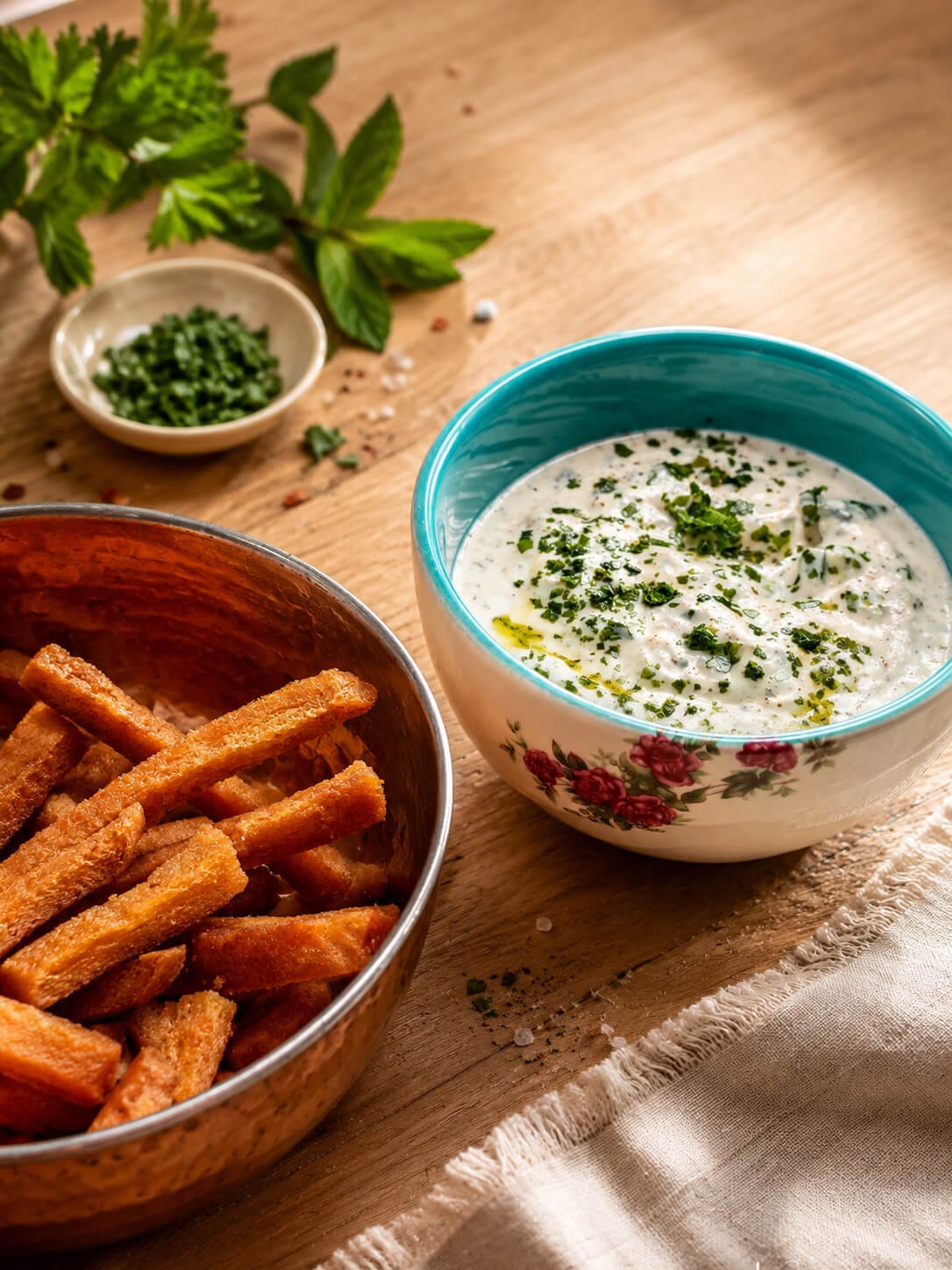 Crispy leftover bread bites served beside mast o khiar topped with herbs and olive oil.