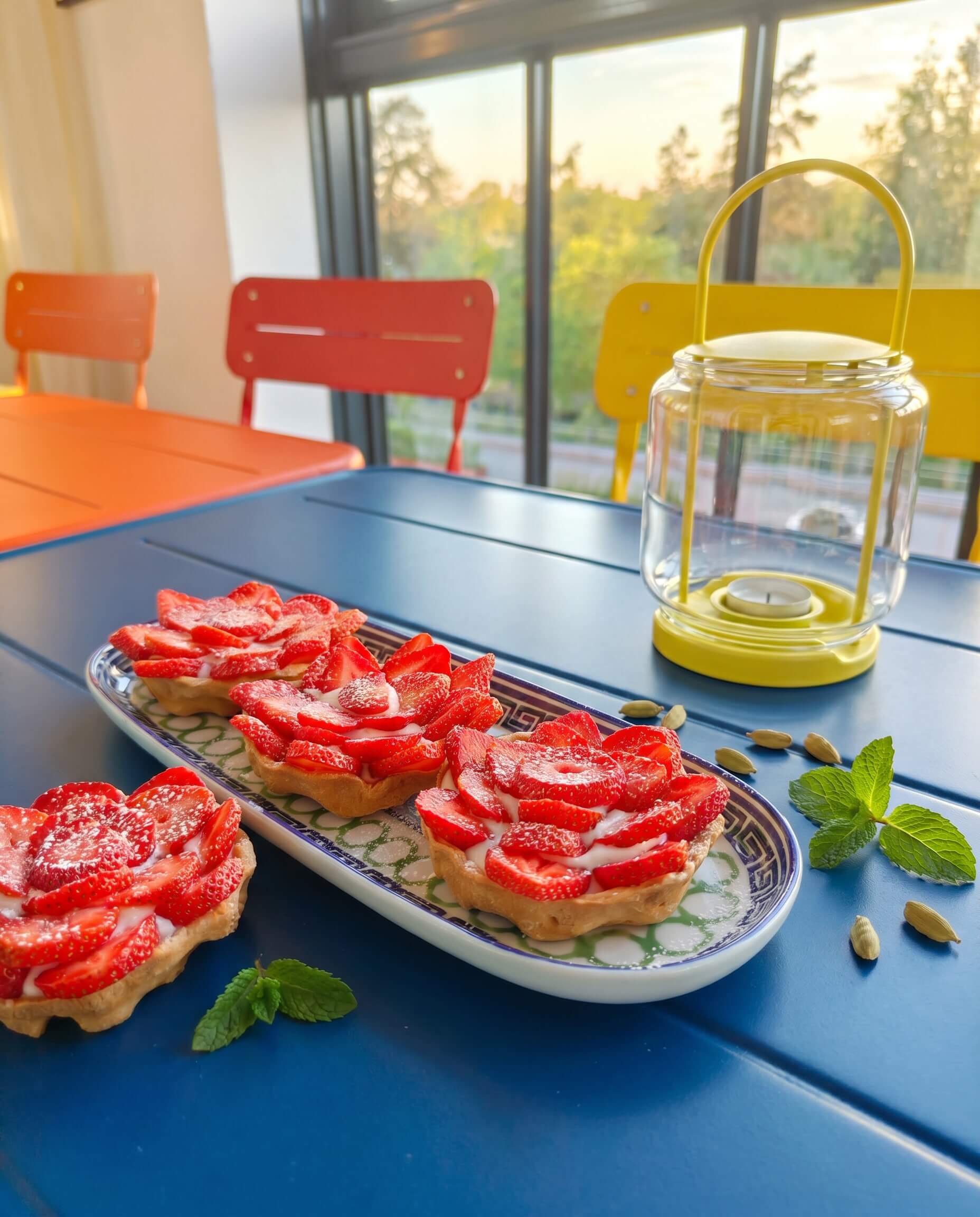 Cardamom strawberry tartlets with vanilla cream served on a blue table with fresh mint, cardamom pods and strawberries.