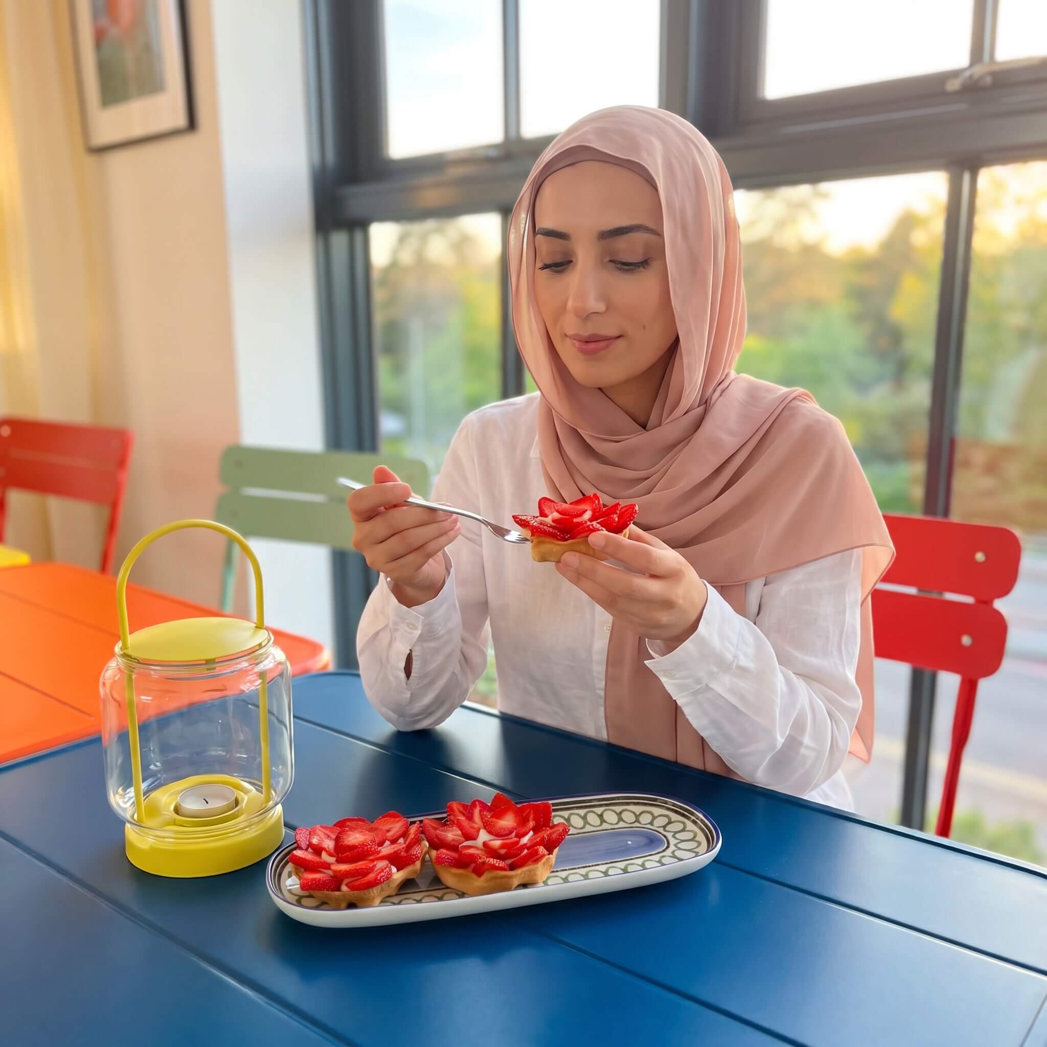 hijabi food blogger enjoying a cardamom strawberry tartlet with vanilla cream at a table beside fresh tartlets.