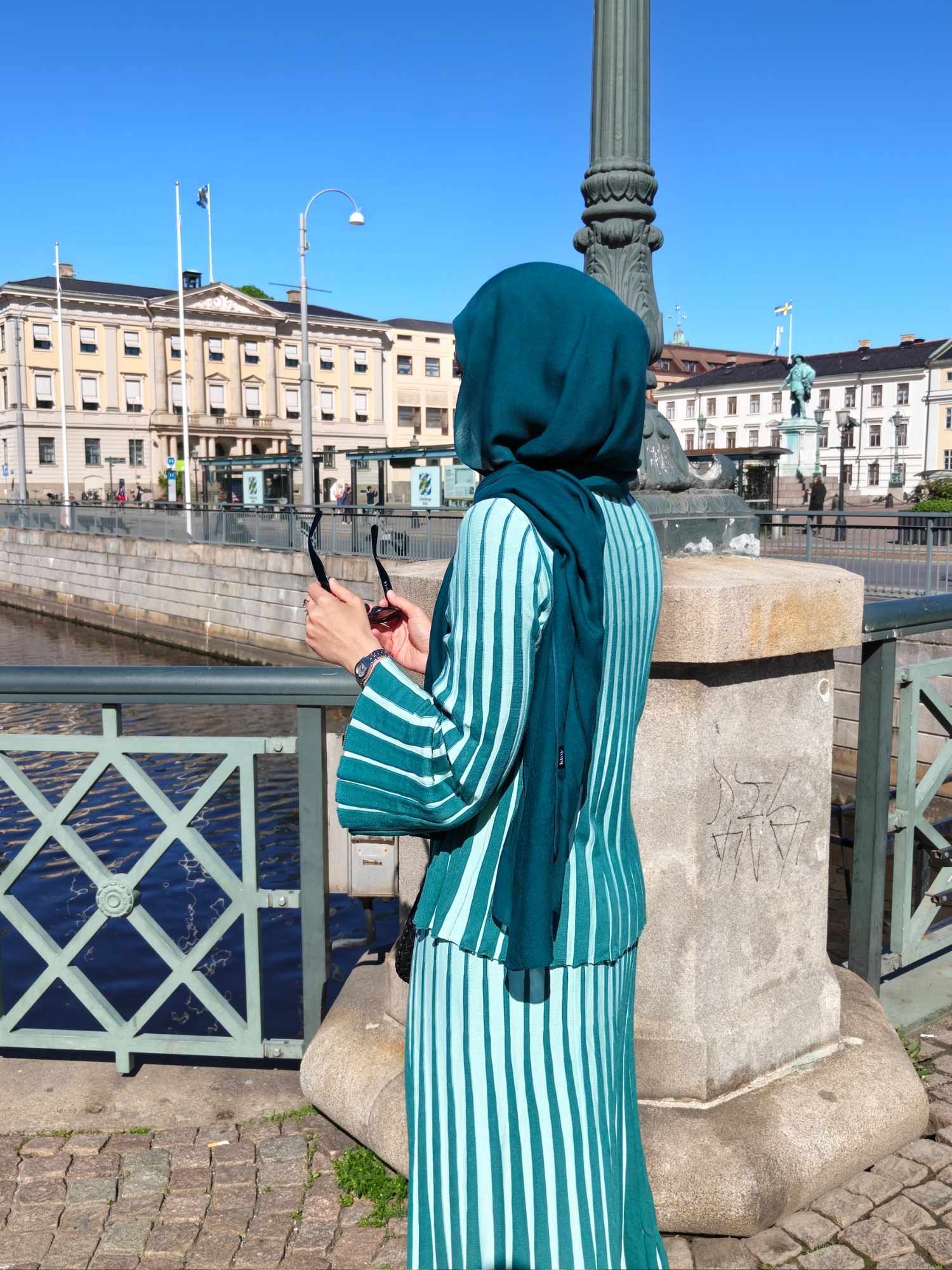 Hijabi woman in a green modest two-piece skirt set with matching hijab by the canal in Gothenburg