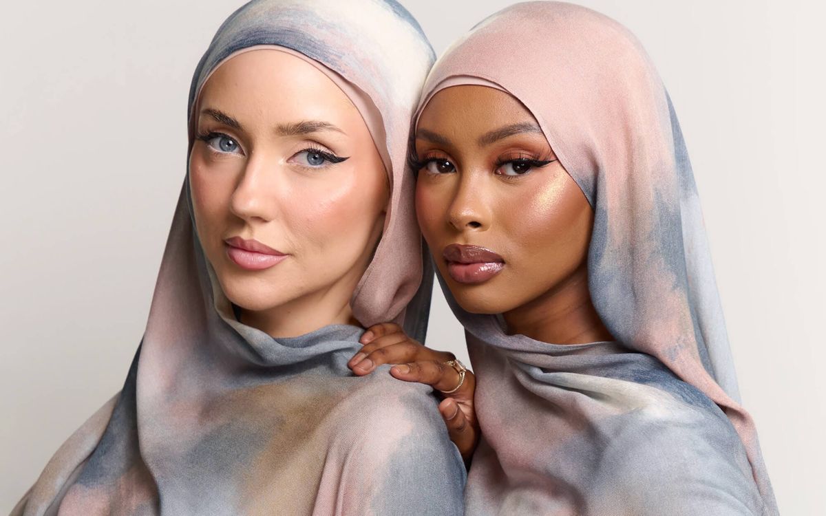 Two women wearing soft marble-patterned modal hijabs in pastel pink, grey, and beige tones, standing closely together against a neutral background.