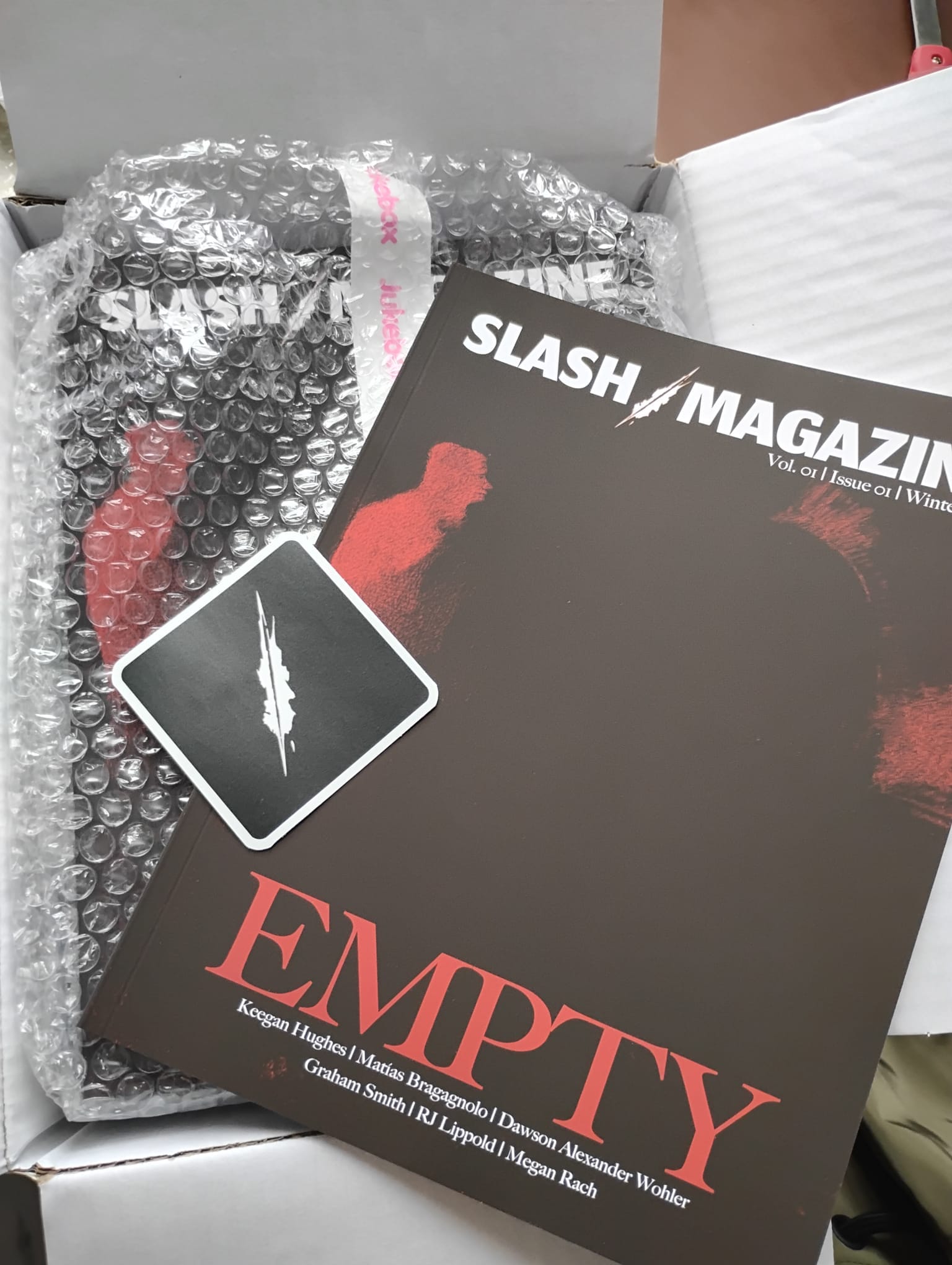 A copy of printed Slash Magazine sits on top of a box of other copies.