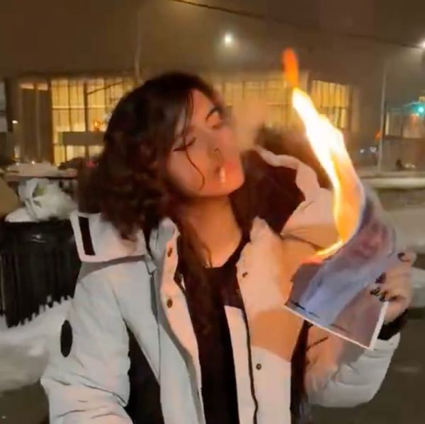 A screenshot from an iconic video showing an Iranian woman lighting a cigarette using a picture of Ayatollah Ruhollah Khomeini
