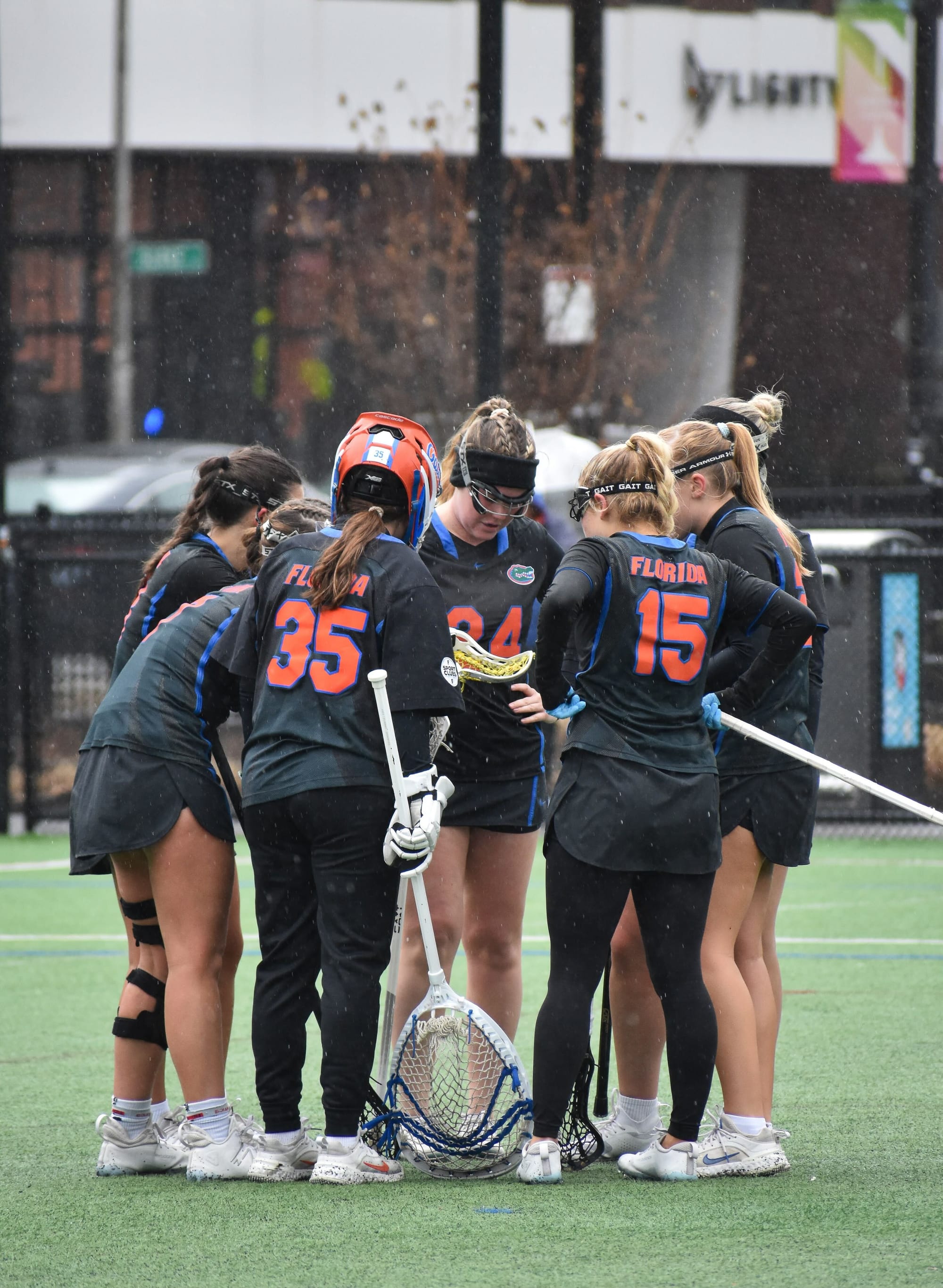 UF club lacrosse discusses game plans in a huddle during a rainy game.