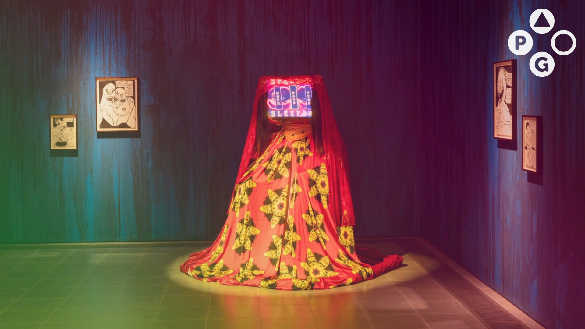 An art installation in a gallery. The piece looks like a sheet draped over a person seated in a chair, but the person's head has been replaced with a box covered in words.