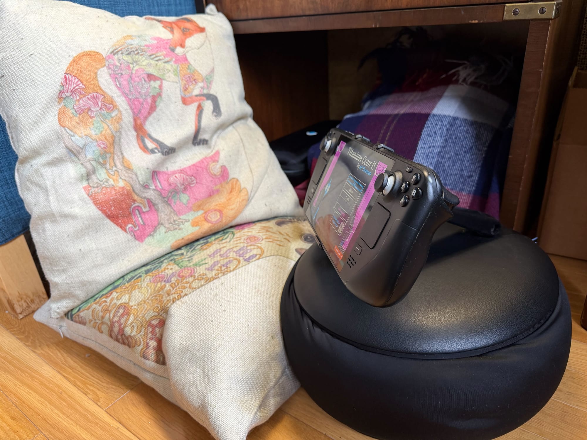 The Mechanism gaming pillow sits with a Steam Deck on it beside two regular throw pillows.