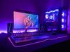 A desk with a gaming setup on it is shown. There's a gaming PC rig with a clear case and RBG lights inside, a monitor, two speakers, a keyboard, and a lightup mousepad.