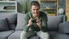 A young person holding a controller sitting on a couch. They have a frustrated but determined expression on their face