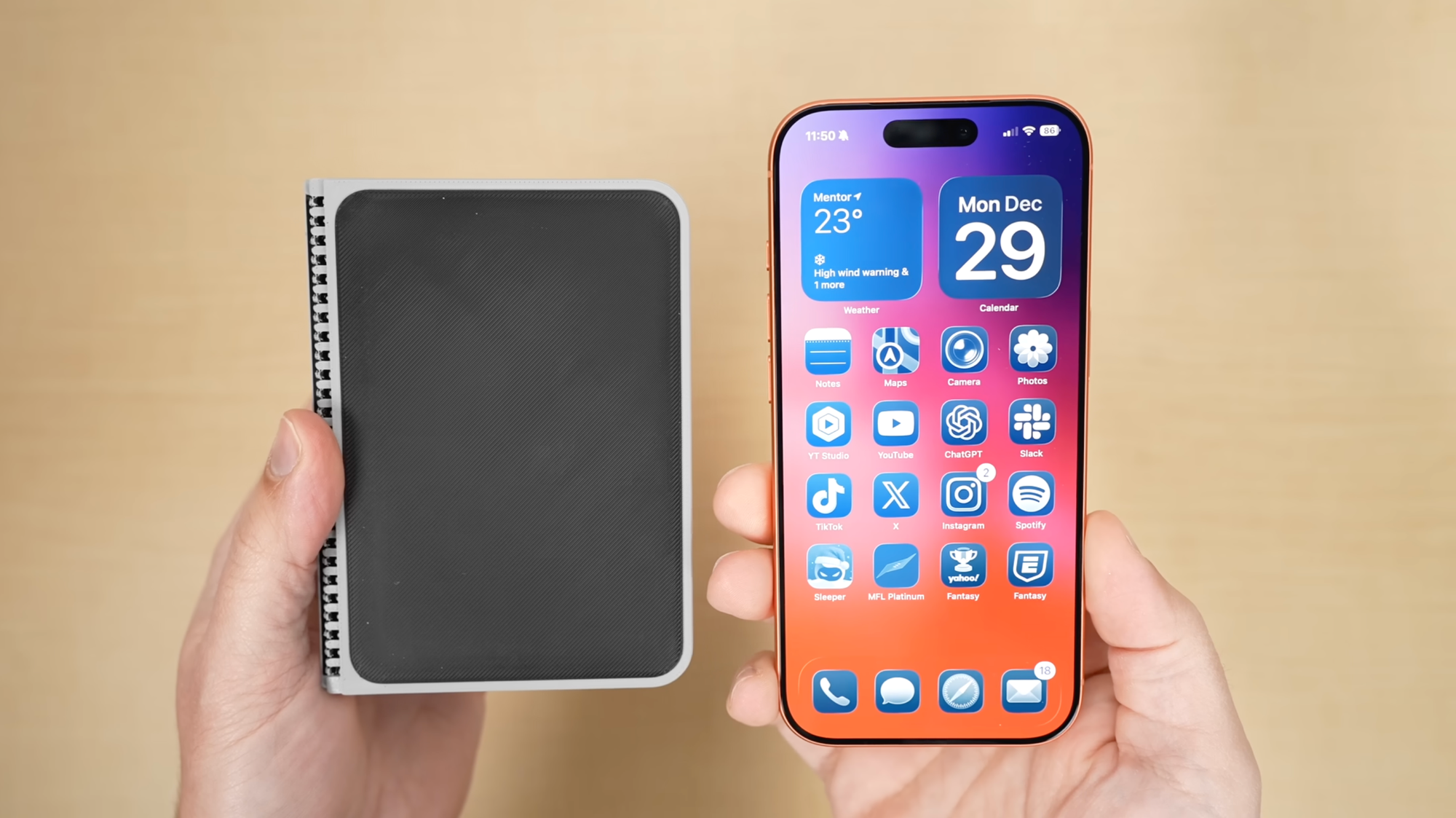 A pair of hands holds the plastic mockup and a real iPhone above a light yellow table from above.
