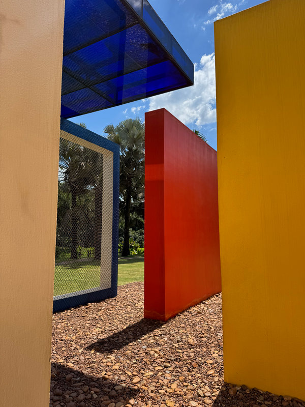 4 colorful squares 4 meters wide stand vertically on a lush green park. Beneath them there are a couple of rocks, creating a art installation in Instituto Inhotim, Minas Gerais, Brasil.