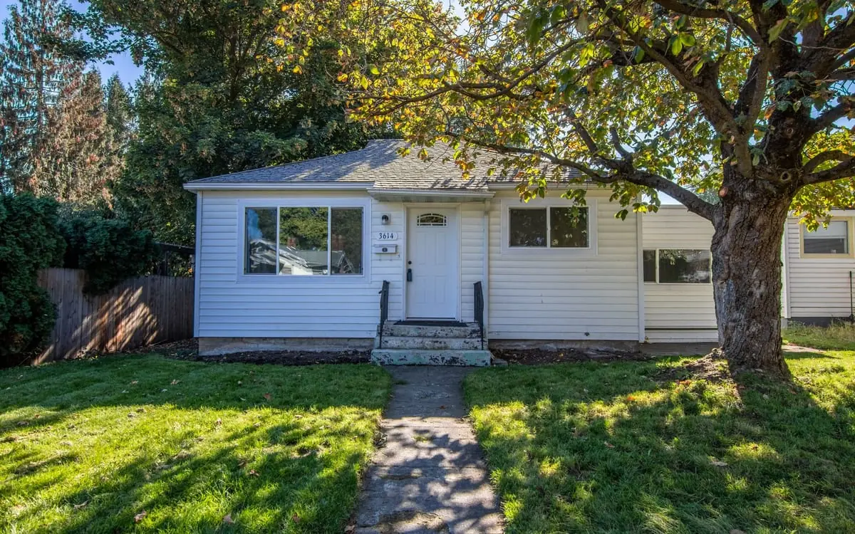 A small single-storey white house with a wide picture window and weathered concrete front steps