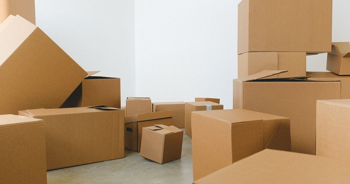 Cardboard moving boxes, some open, stacked on a concrete floor in an empty white room