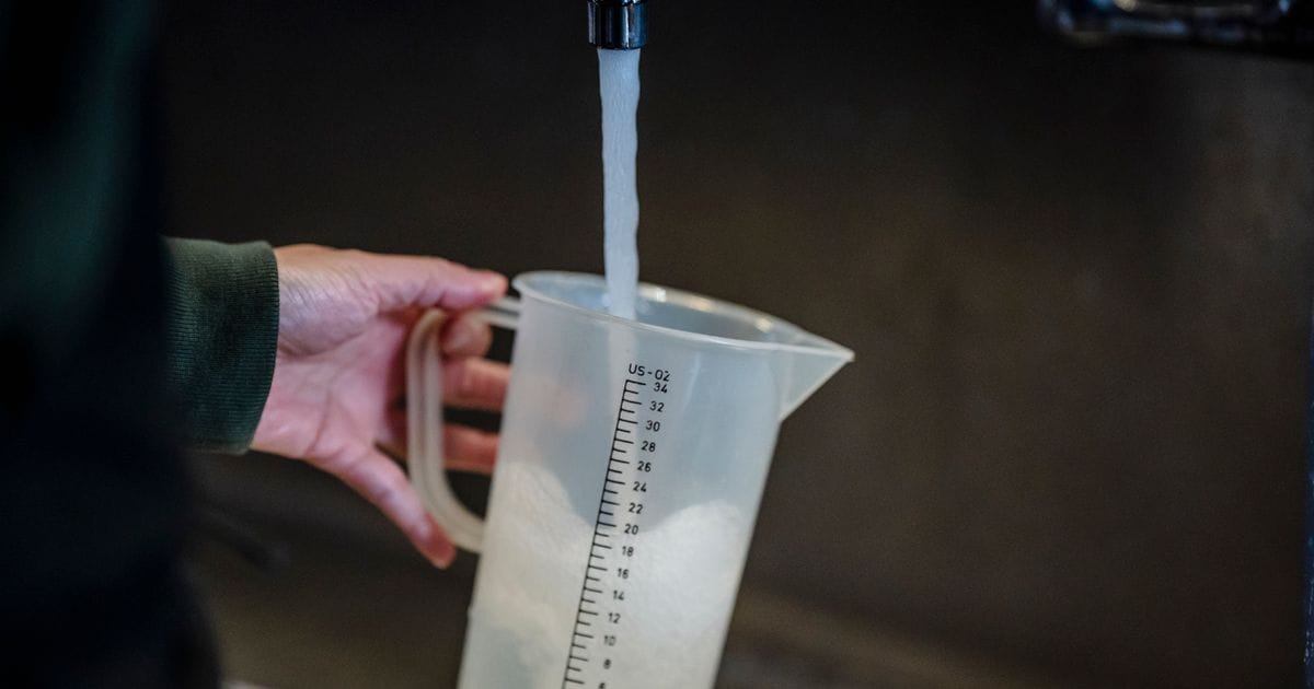 Hand holding a plastic measuring pitcher under a running faucet
