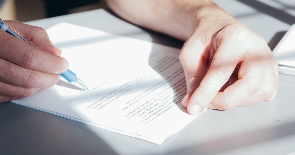 Close-up of a hand signing a printed document with a blue pen on a gray table