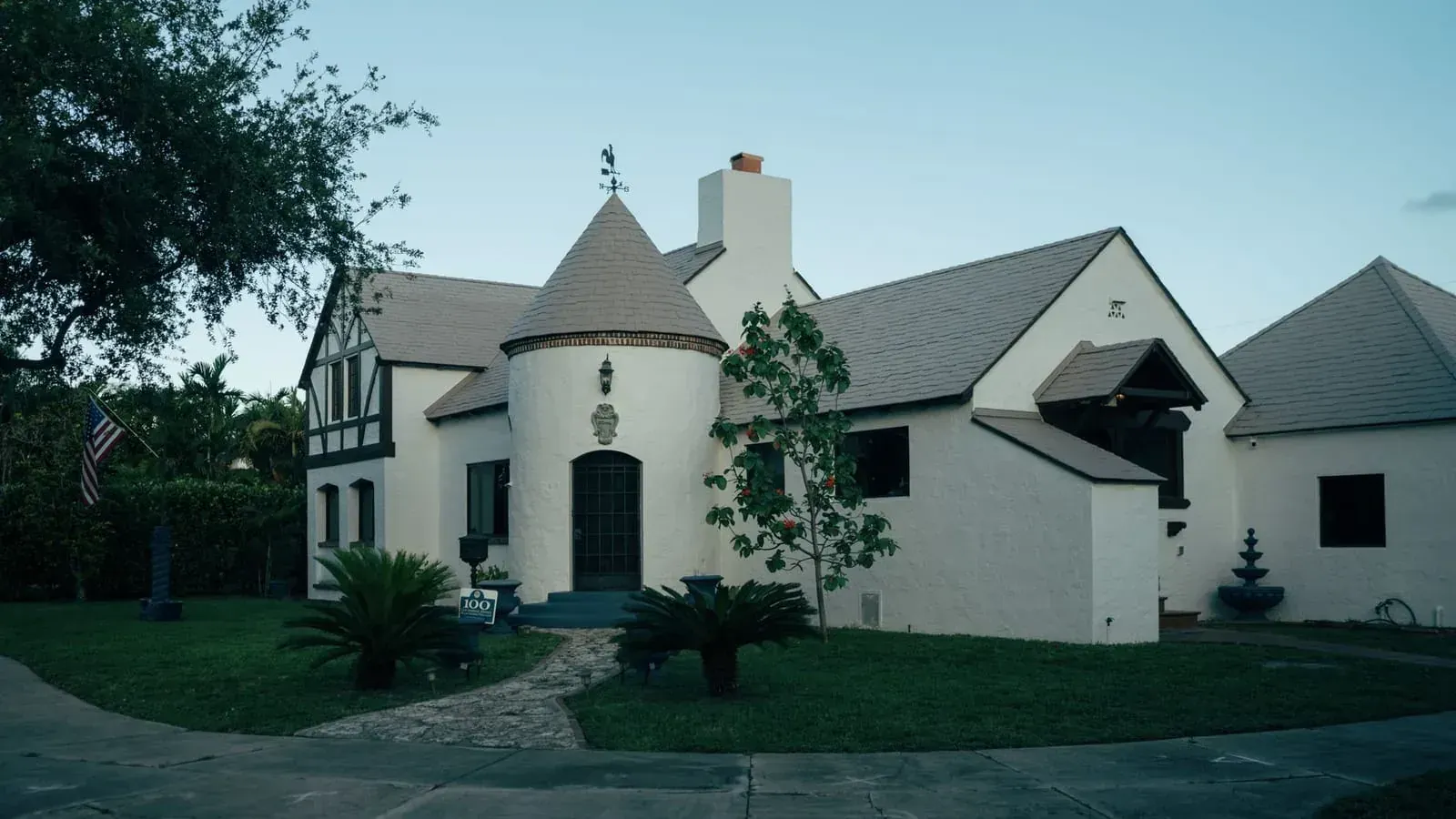 A white stucco house with a conical turret over the entrance and palms in the front garden
