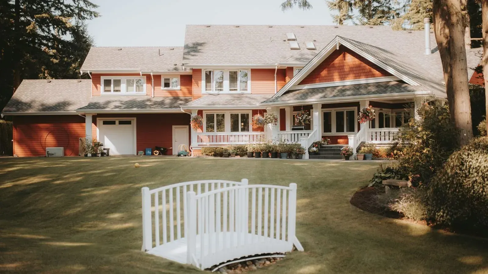 A large red-sided family home with a wraparound porch and hanging flower baskets