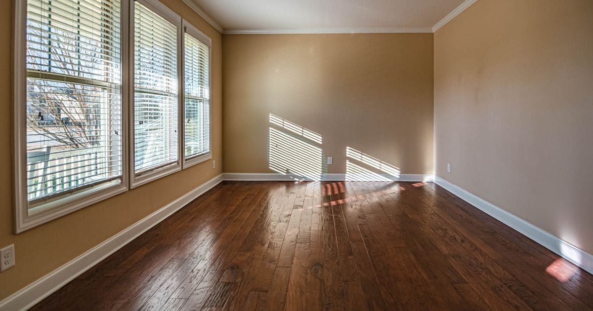 Empty room with tan walls, dark wood floors and sunlight coming through window blinds