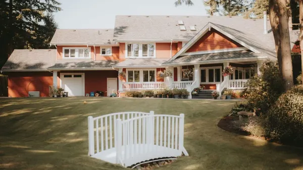 A large red-sided family home with a wraparound porch and hanging flower baskets