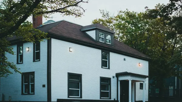 A white two-storey colonial house with a dark roof and a columned entry porch, lit at dusk
