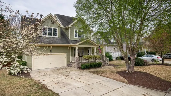 A green two-storey house with a two-car garage and a dogwood in flower, on a suburban street