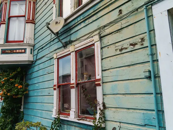Peeling blue clapboard siding around a pair of red-trimmed windows on an older house