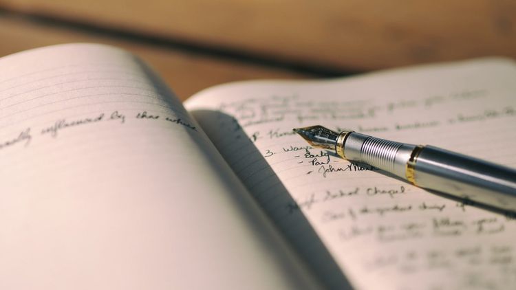 fountain pen lying on an open notebook with pages full of writing
