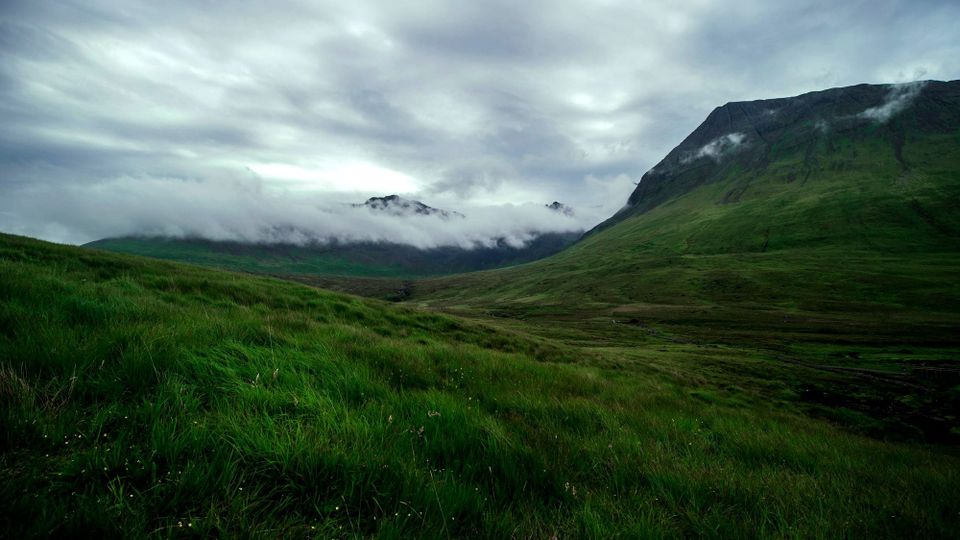 cloud covered mountain in the distance with a grassy valley in the foreground